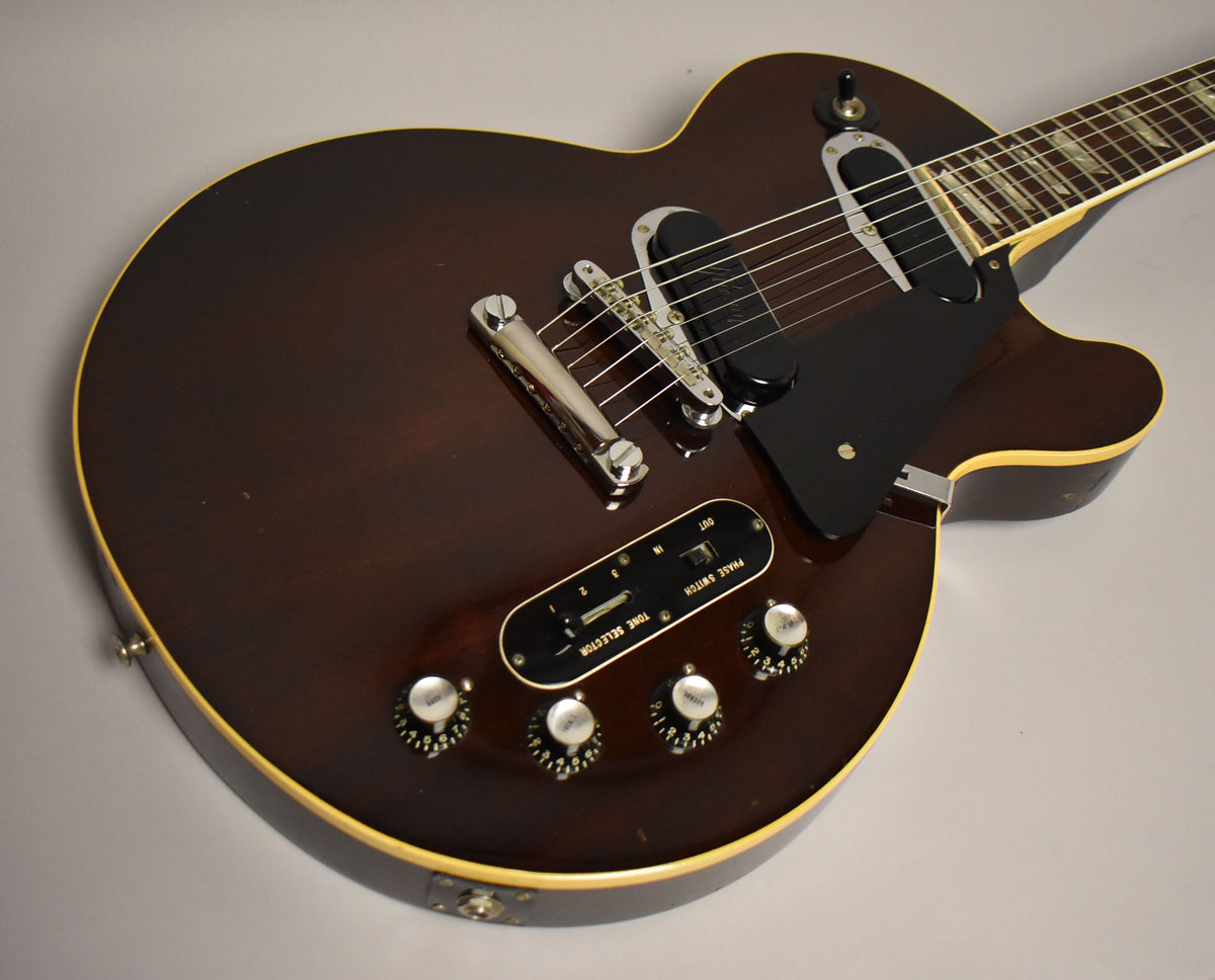 Dark walnut guitar body with cream binding, four control knobs, two slider switches, and a black pickguard.