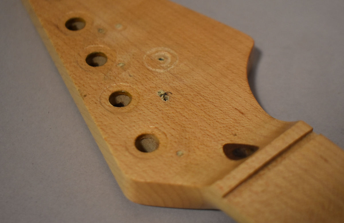 Close-up of a light maple Stratocaster headstock with four tuner holes, a visible string tree screw hole, and a truss rod access.