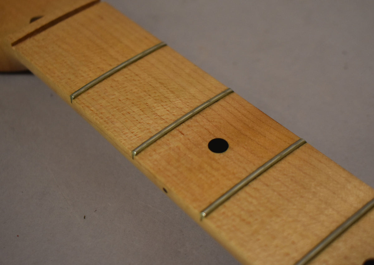 Close-up of the maple fretboard, showing light wood grain, silver frets, and a single black dot inlay at the 7th fret.