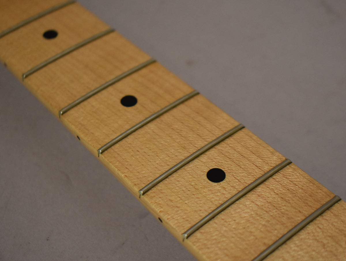 Close-up of a light maple fretboard with dark dot inlays and shiny frets, viewed at an angle from the lower left.