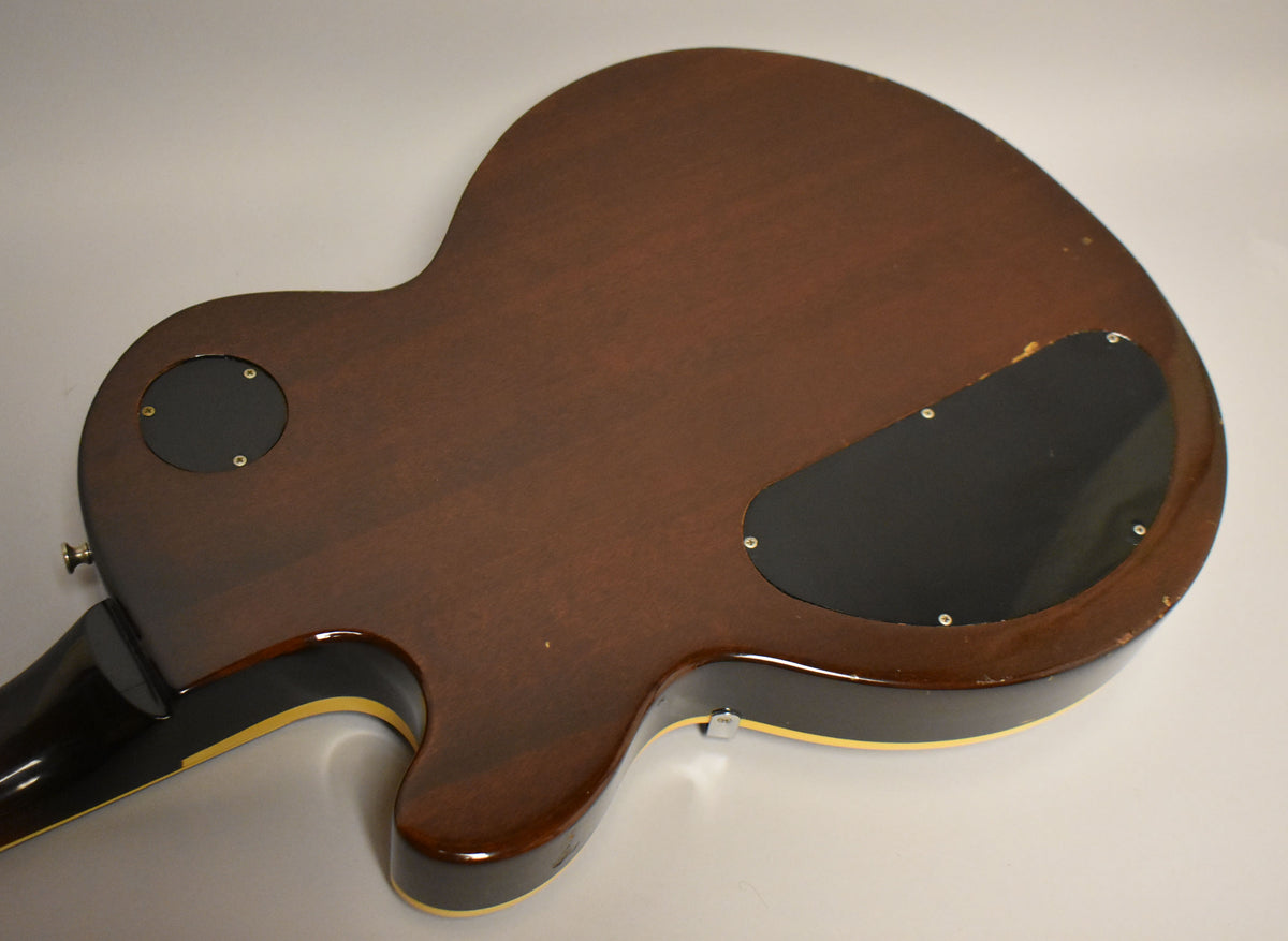 The guitar's dark walnut back, showing two black control cavity covers, has visible finish wear and checking on the lower bout.