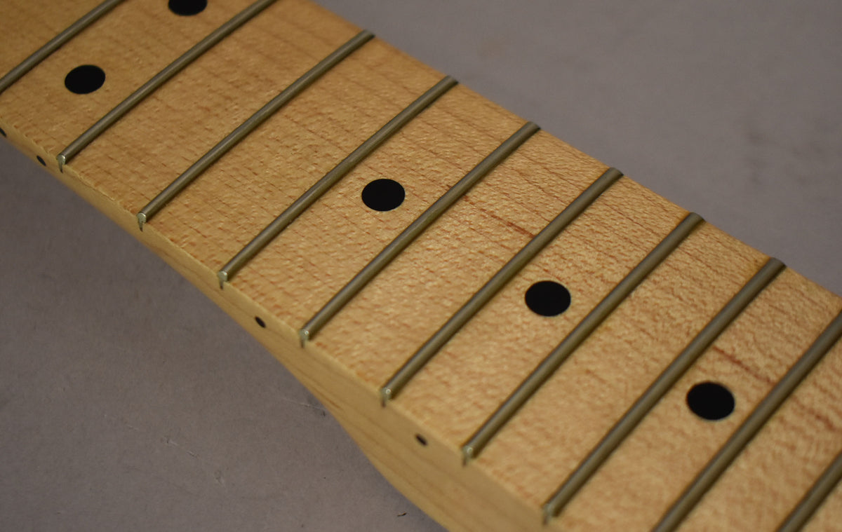 Close-up of a light maple fretboard with black dot inlays and shiny frets, viewed diagonally from the nut end.