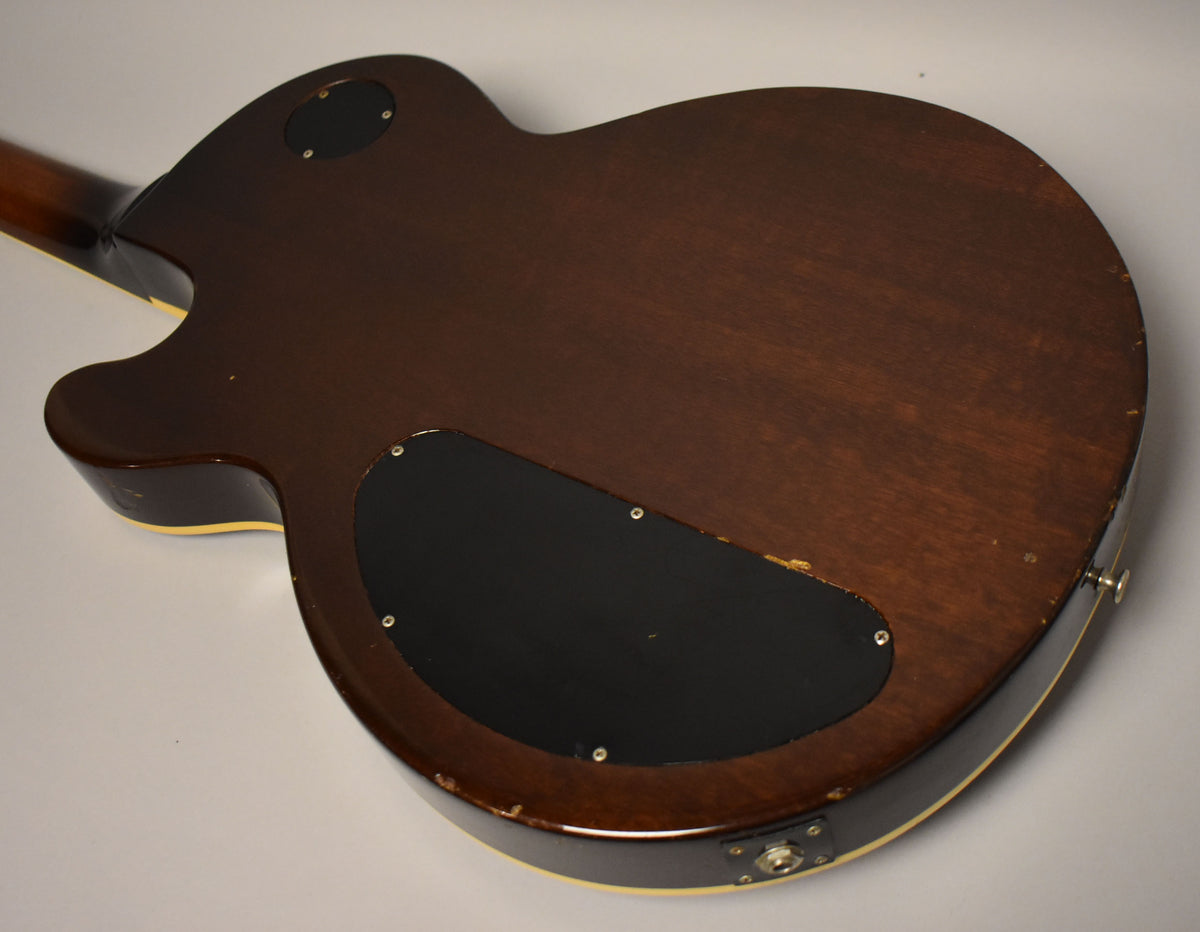 The back of a dark walnut guitar body, showing two black control cavity covers and wear along the cream binding.