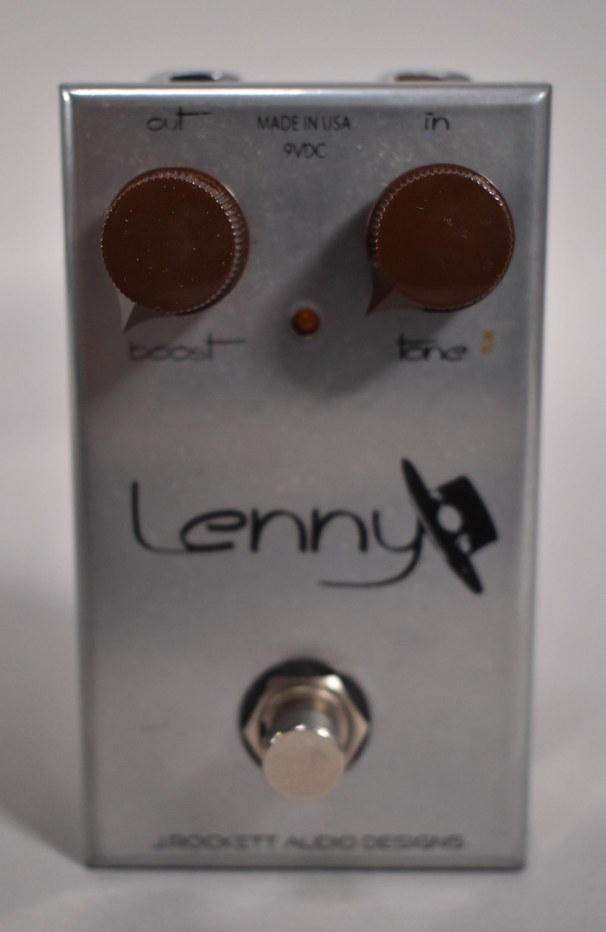 A silver effects pedal, viewed from the front, with two brown knobs, an orange LED, and a chrome footswitch.