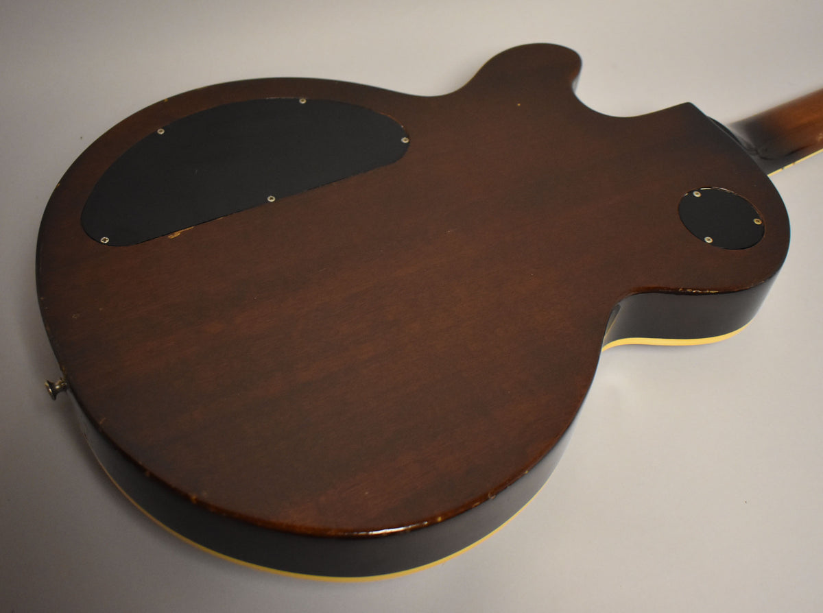 The back of the walnut-finished guitar body, showing a large black control cavity cover and a smaller circular cover, with some edge wear.