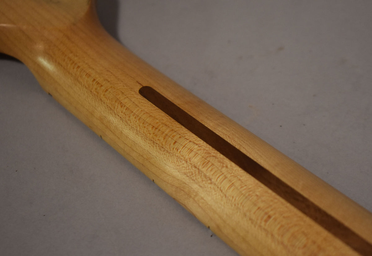 The back of a light maple neck with a dark brown skunk stripe, showing subtle flame figuring and a few small dark marks.
