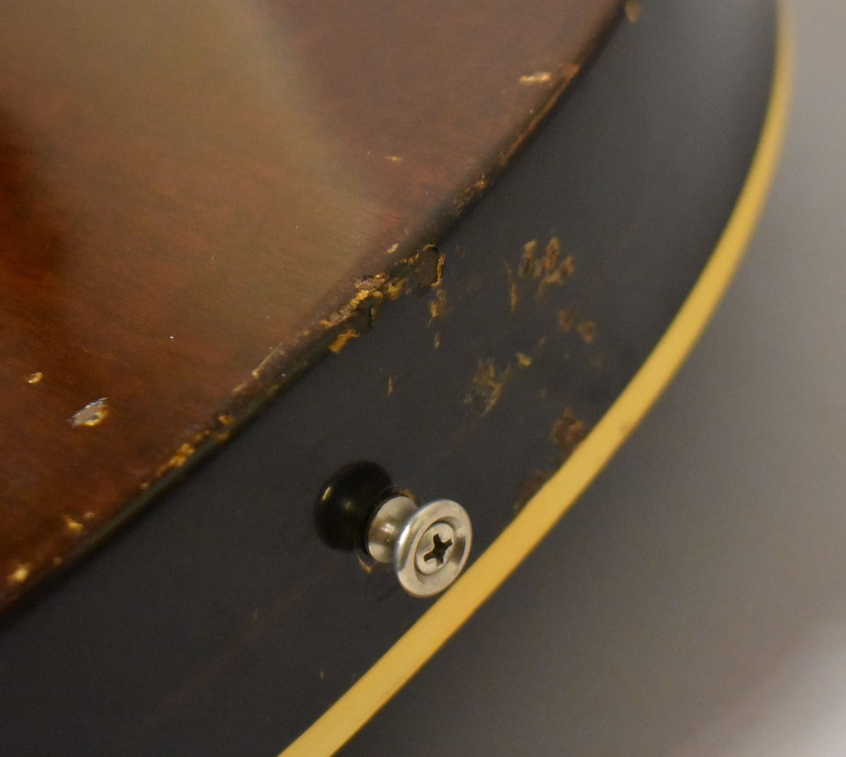Close-up of the guitar's lower bout, showing a black strap button, heavy wear and chipping on the dark walnut finish, and cream binding.