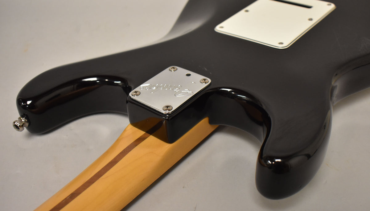 The black guitar body's back is angled, showing the neck joint with a chrome plate, a white backplate, and light surface scratches.