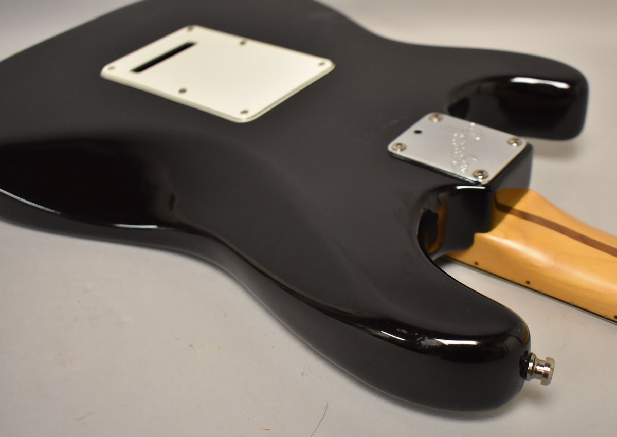 The black guitar body's lower back is visible, showing a white tremolo cover, chrome neck plate, and strap button with finish wear.