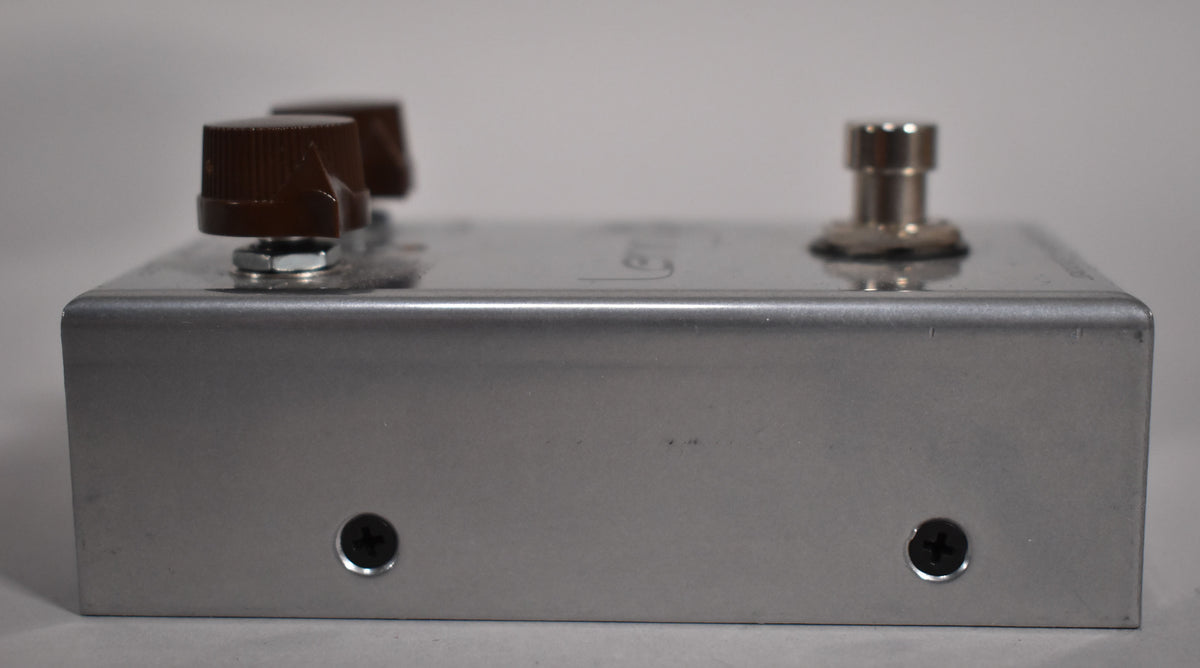 Side view of a brushed silver pedal with two brown knobs and a silver footswitch on top, showing minor scuffs.