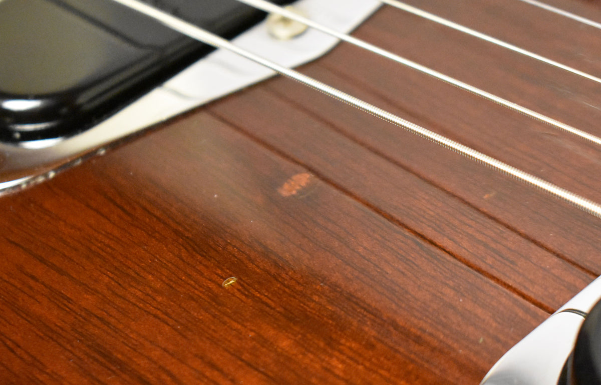 Close-up of the dark walnut body, showing a small, lighter brown wear spot and a tiny yellow speck near the strings.