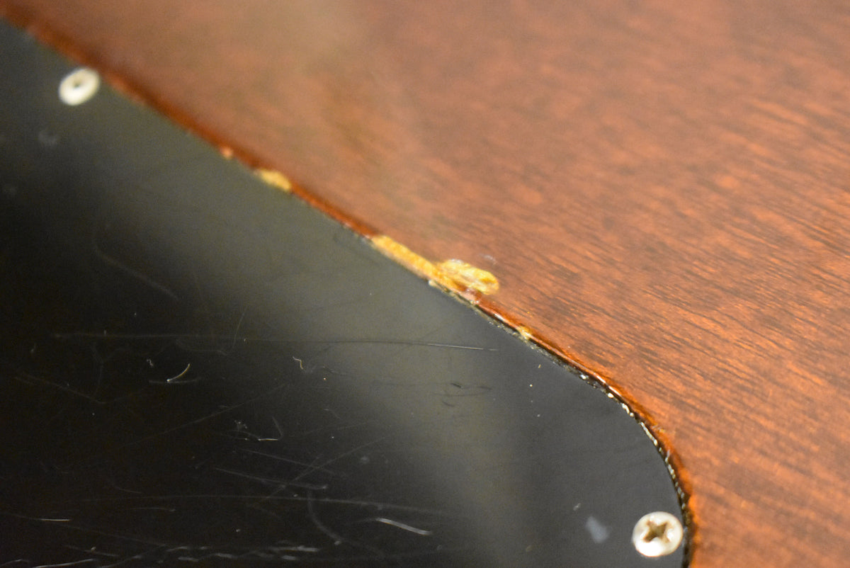 Close-up of the guitar's back, showing the edge of a black control cavity cover with two screws and glue residue along the seam.