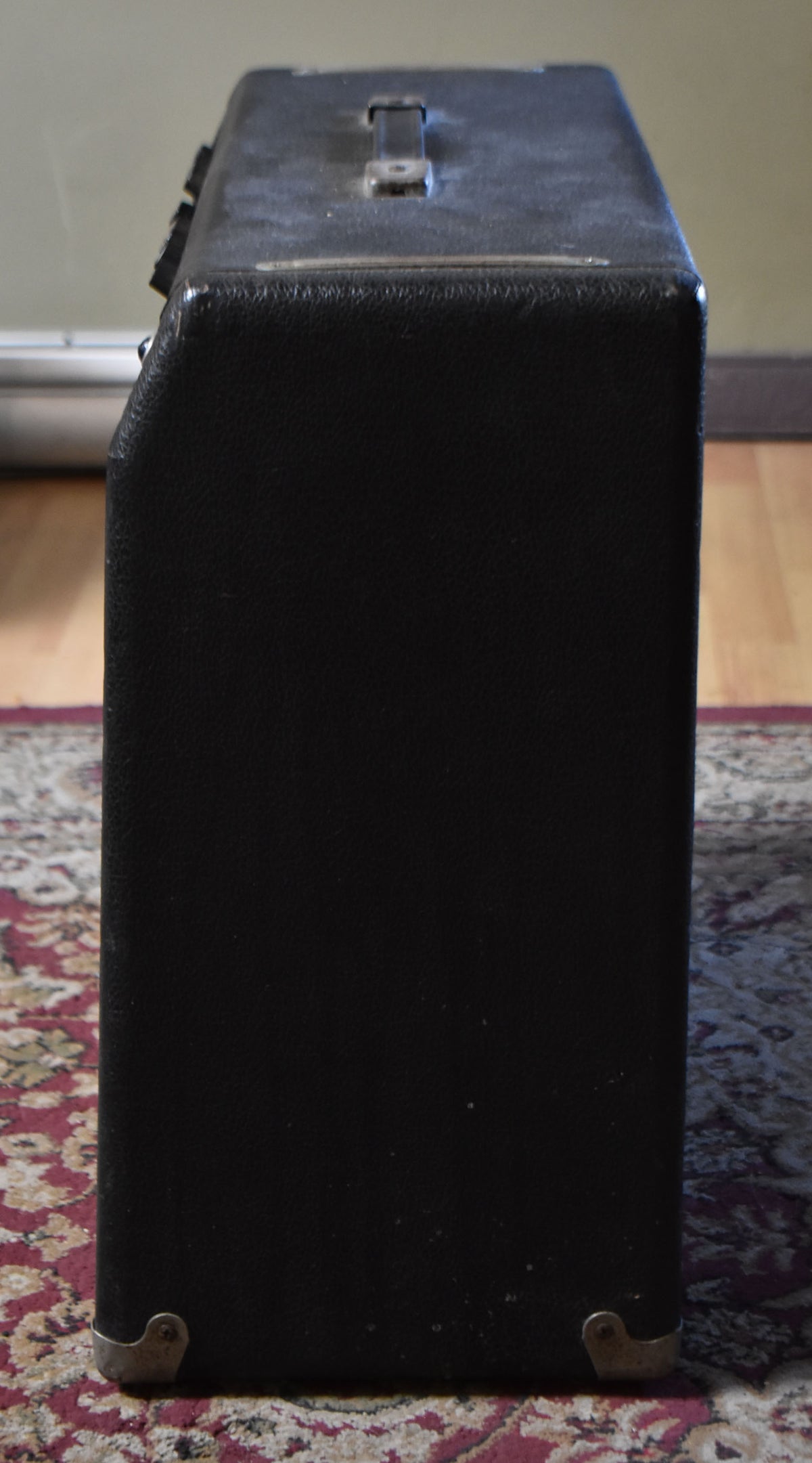 Right side view of a black textured amplifier, showing a worn top handle, control knobs on the left, and two metal corner protectors.