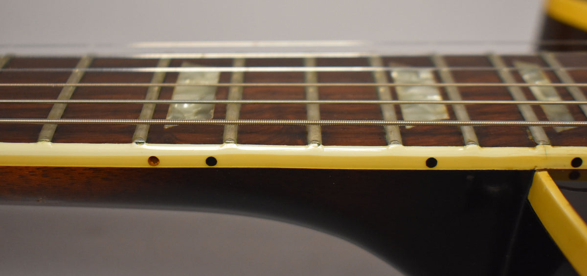 Close-up of the dark rosewood fretboard with trapezoid inlays, showing the cream binding and side dots, with some wear on the frets.
