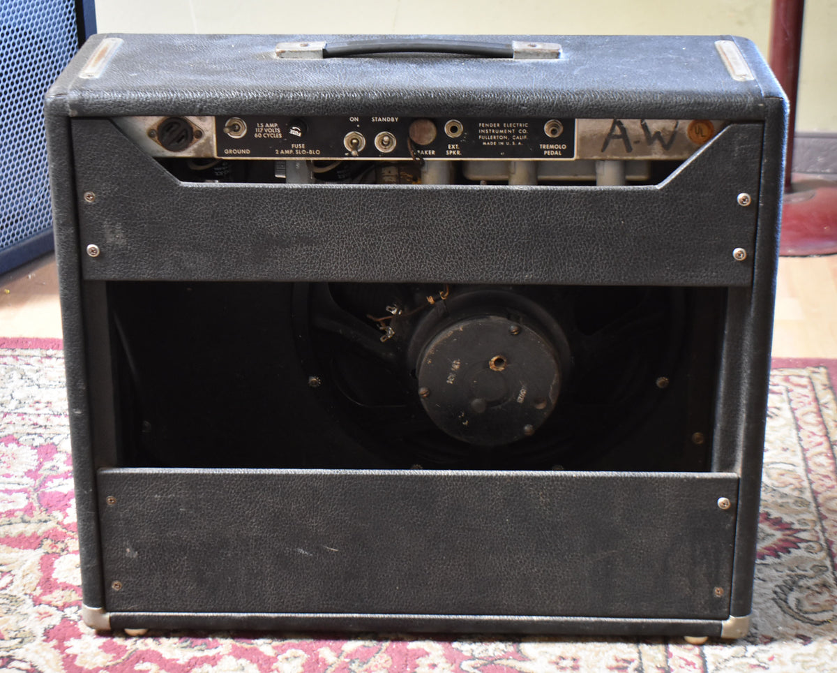 Rear view of the black tolex combo amp, showing the open back with a visible speaker, control panel, and worn handle.