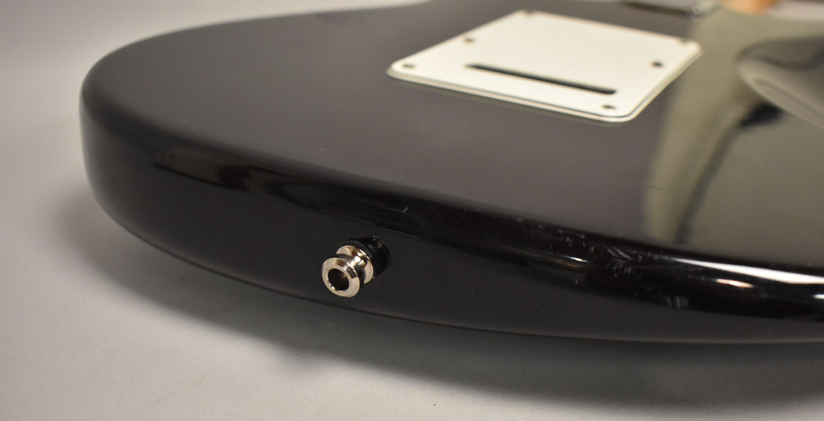 Close-up of the black guitar's lower bout, showing the chrome output jack and a white tremolo cover on the back.