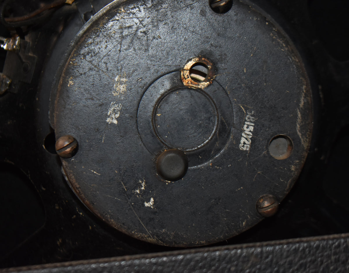 Close-up of the speaker's worn black magnet cover, showing mounting screws, a central cap, and a partially visible serial number.