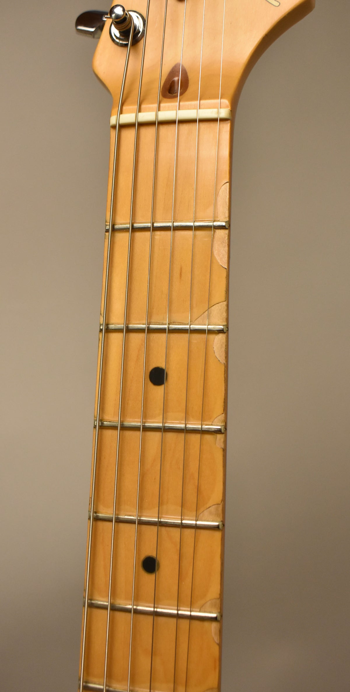 Close-up of the maple fretboard and headstock, showing wear and chipping of the finish along the edges and around the frets.