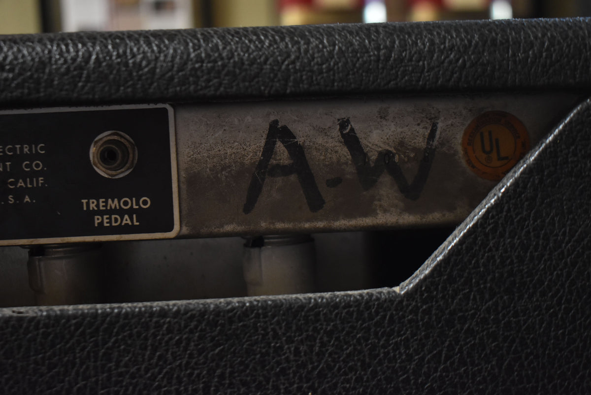 Close-up of the amp's black textured Tolex covering and worn silver control panel, showing a "Tremolo Pedal" jack and "A-W" written in black marker.