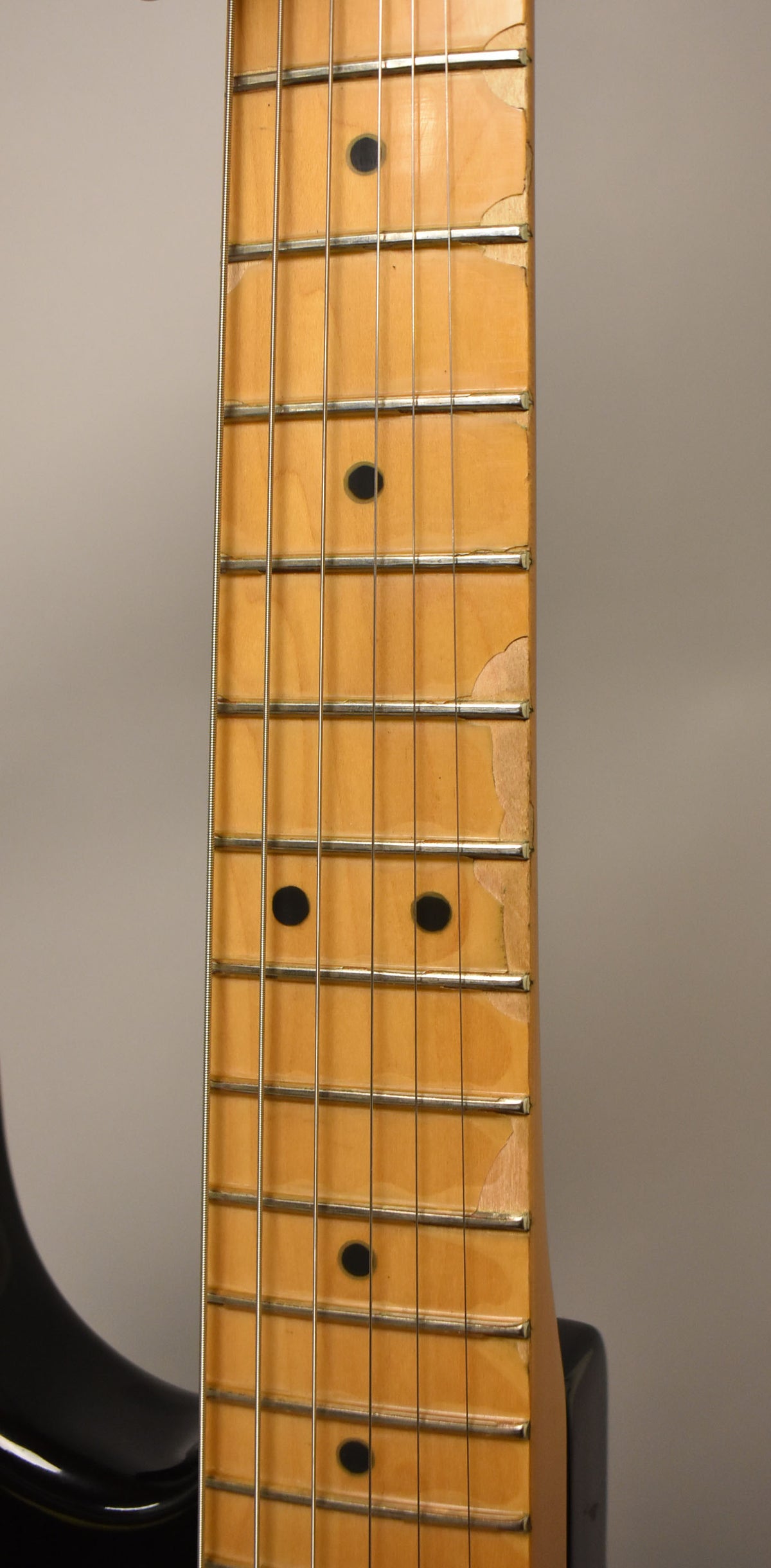 Close-up of the maple fretboard, showing significant lacquer wear and chipping along the bass side edge, revealing lighter wood beneath.
