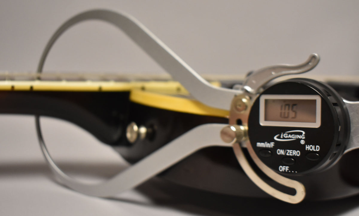 A digital caliper measures the fret height on the dark walnut neck, showing "1.05" on its display.
