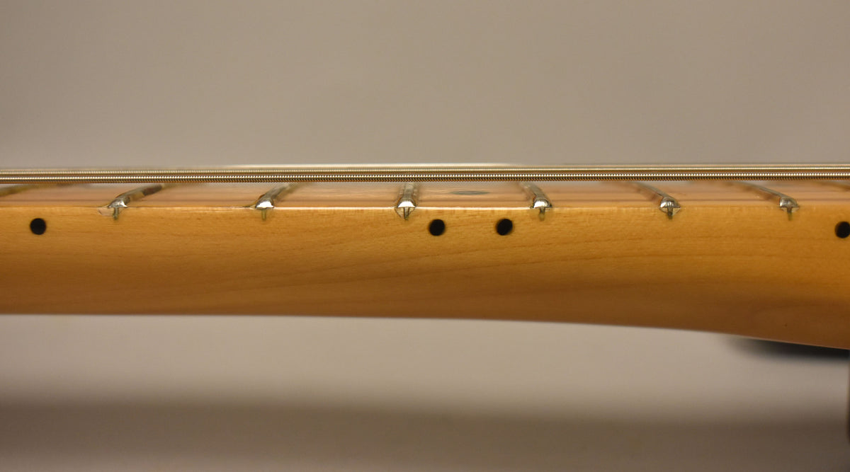 Close-up of the maple fretboard with visible fret wear, black dot inlays, and strings running above.