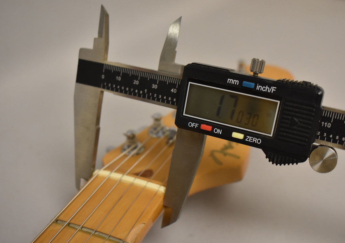 A close-up of the guitar's headstock and nut, with digital calipers measuring the nut width at 1.7030 inches.