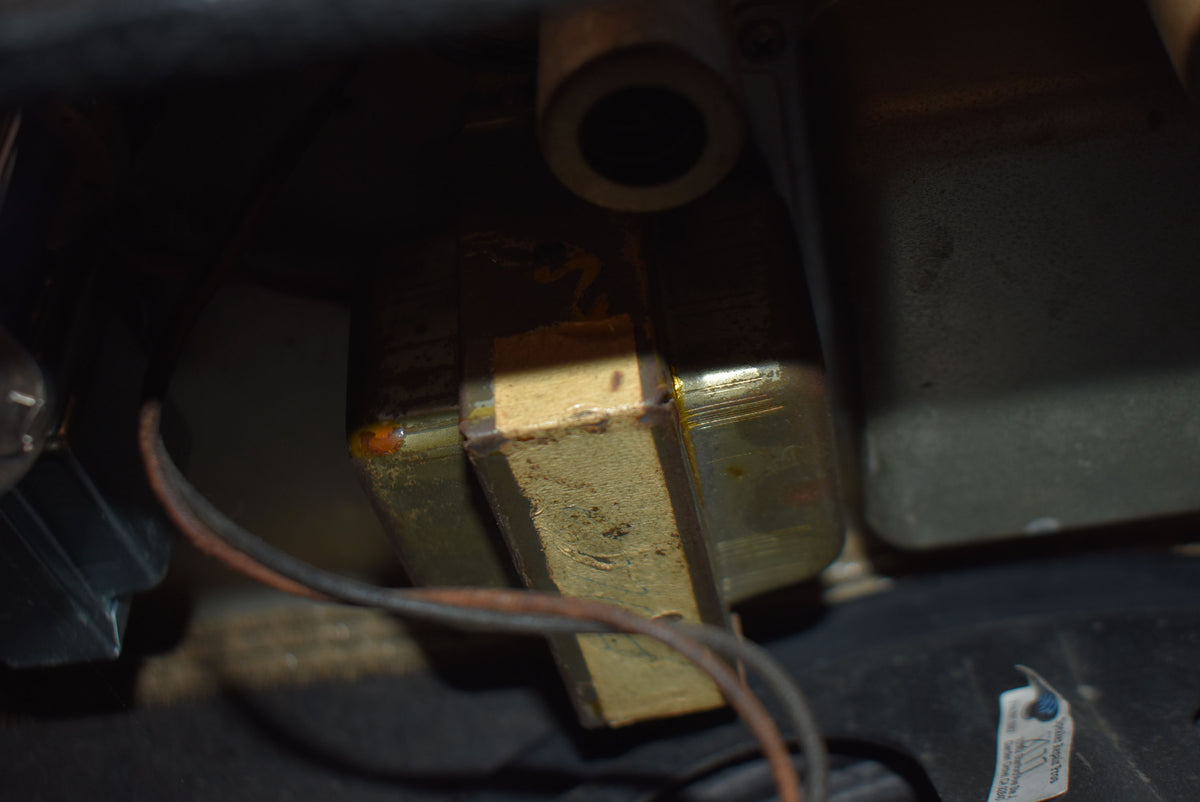 A close-up of internal components, showing a rectangular metal transformer with a worn, light brown paper wrap and visible wiring.
