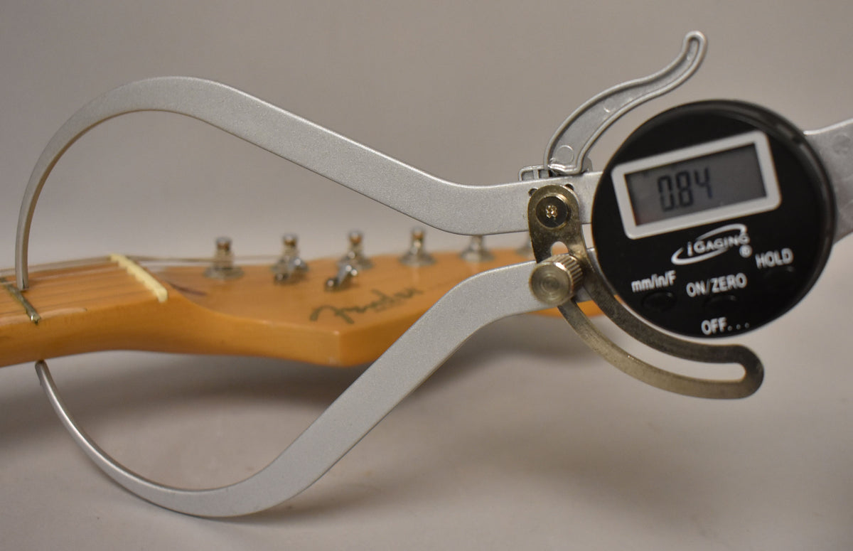 A digital caliper measures the guitar's headstock, displaying "0.84" on its screen.