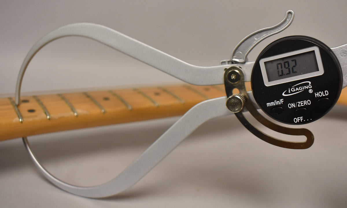 A digital caliper measures the maple fretboard and frets, showing a reading of 0.92, with some wear visible on the fretboard.
