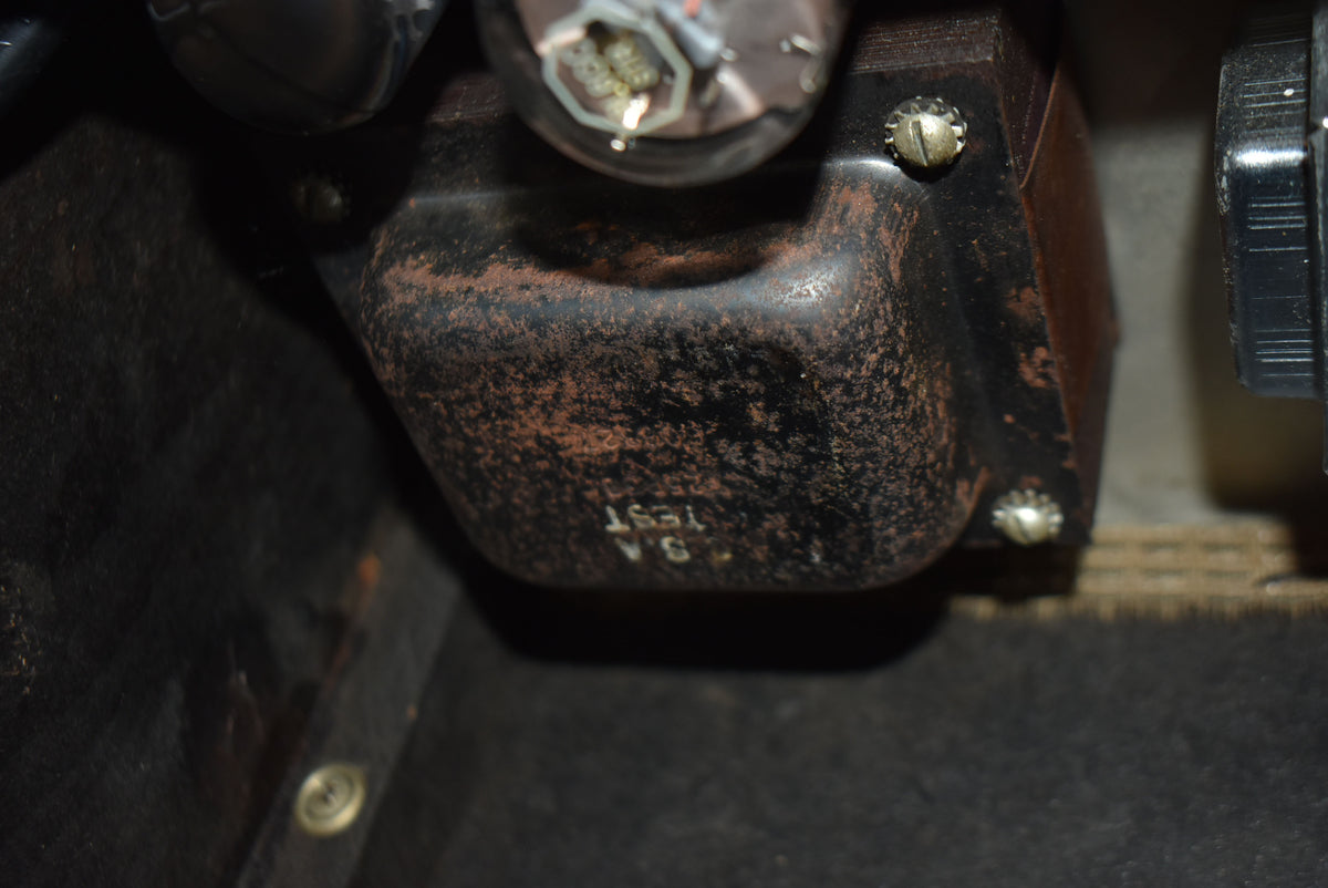 A close-up of the amplifier's black metal transformer, showing heavy rust and a visible vacuum tube above it.