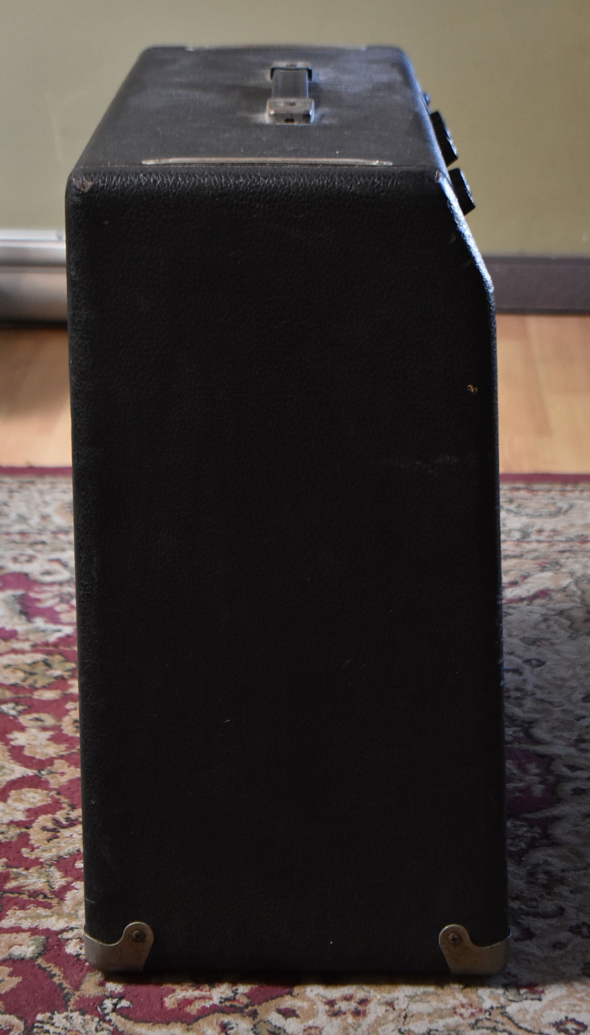 The black tolex amplifier is seen from the right side, showing a top handle, two visible knobs, and metal corner protectors.