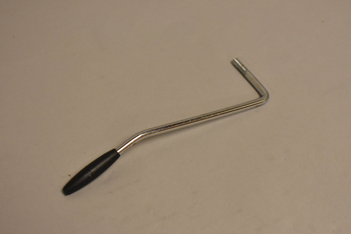 A chrome tremolo arm with a black tip, showing some wear and tarnishing on the metal, is angled against a light grey background.
