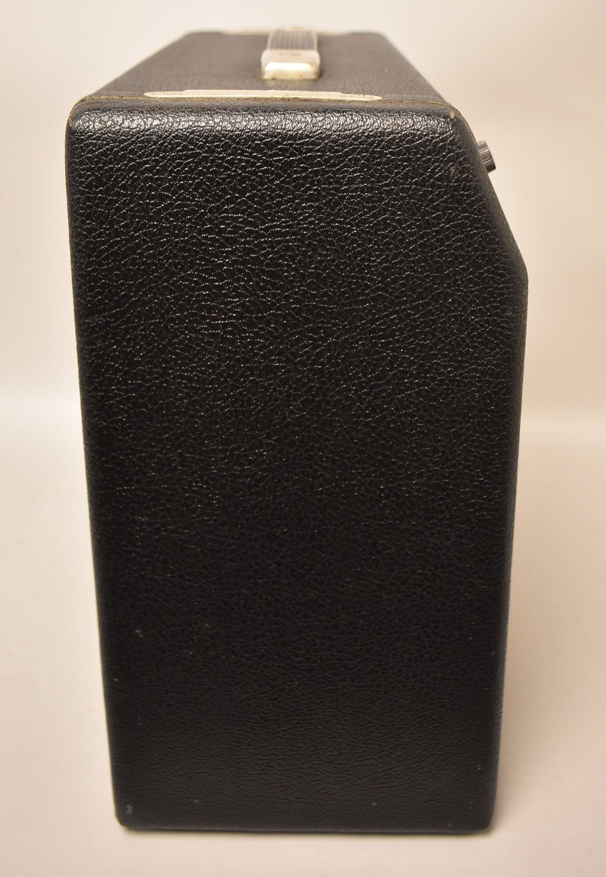The black textured tolex amp is viewed from the right side, showing a top handle and a single control knob.