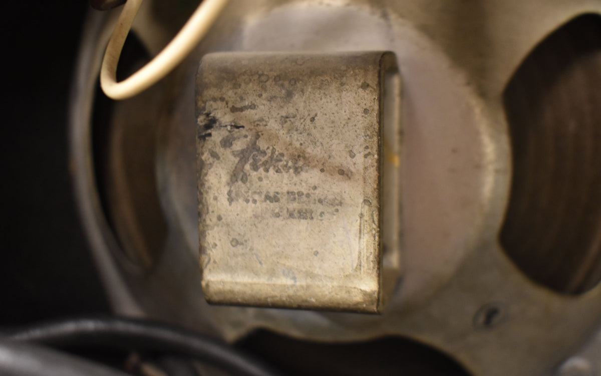 Close-up of a tarnished, rectangular metal component with visible pitting and wear, mounted on a speaker magnet.