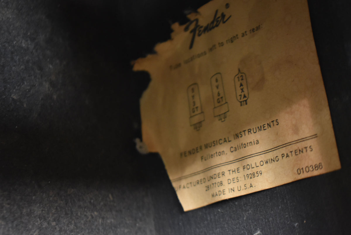 Close-up of a worn, tan paper label with tube diagrams and patent info, partially peeling from the black interior of the amp.