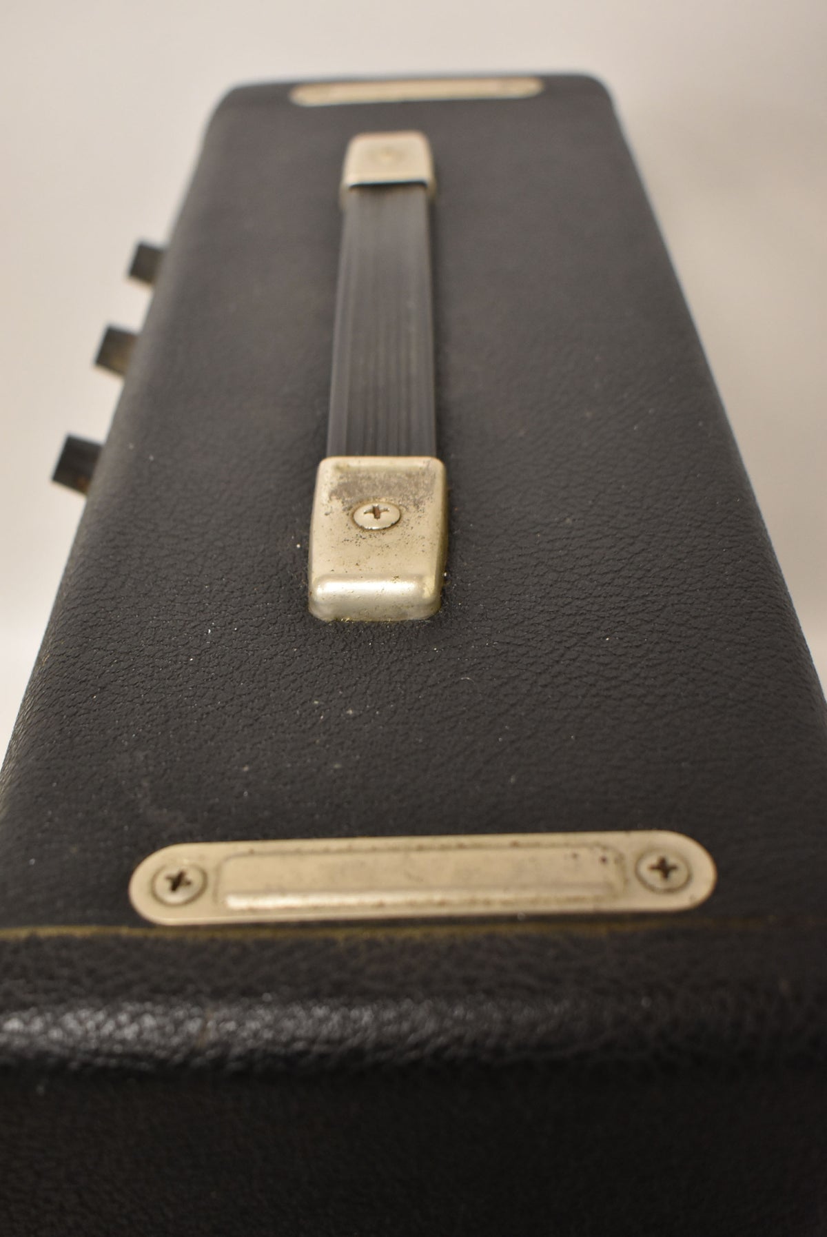 Top-down view of the black textured amp, showing its worn silver-colored handle and a metal plate with two screws.