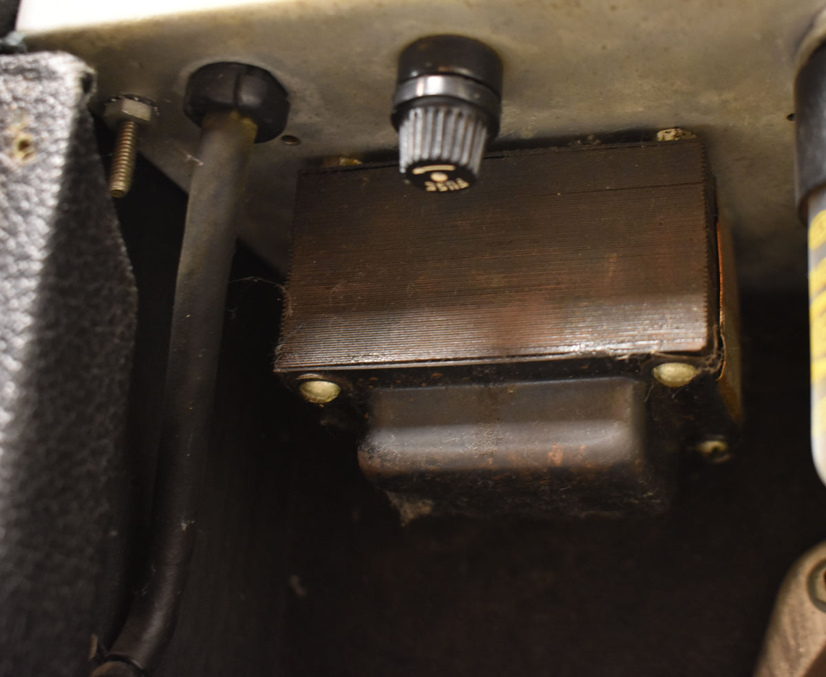 A close-up of the amp's internal components, showing a dark brown transformer, a black fuse holder, and some dust and cobwebs.