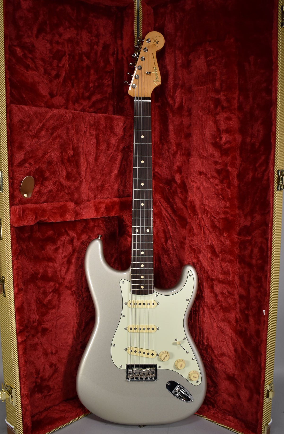 Full-length view of a silver Stratocaster with a light pickguard, three cream pickups, and a rosewood fretboard, in a red velvet case.