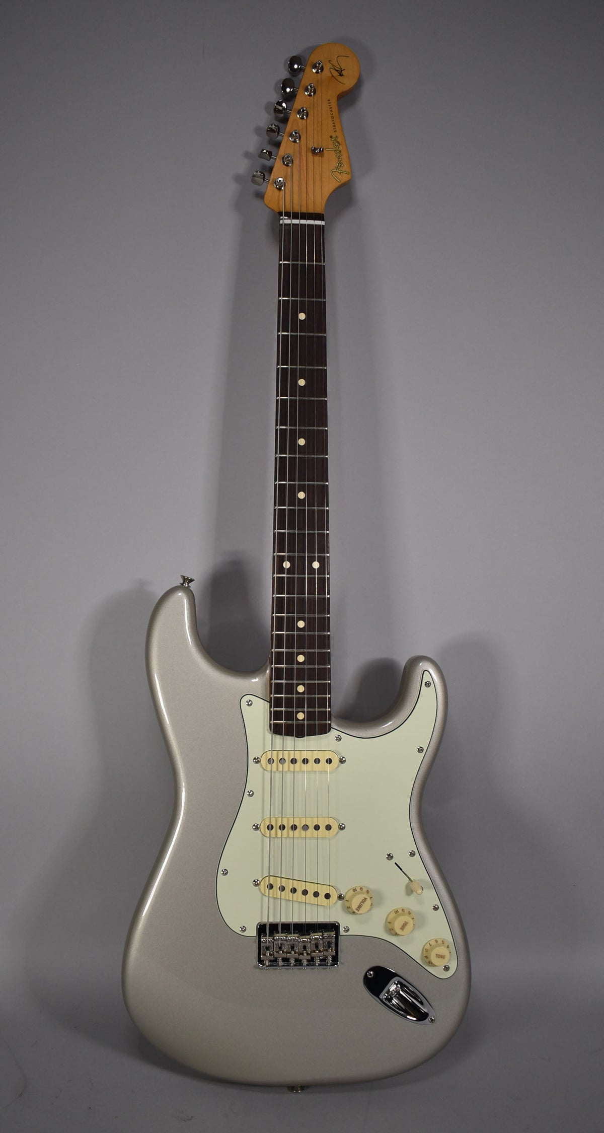 Full front view of a silver Stratocaster with a light mint green pickguard, three cream single-coil pickups, and a chrome tremolo bridge.