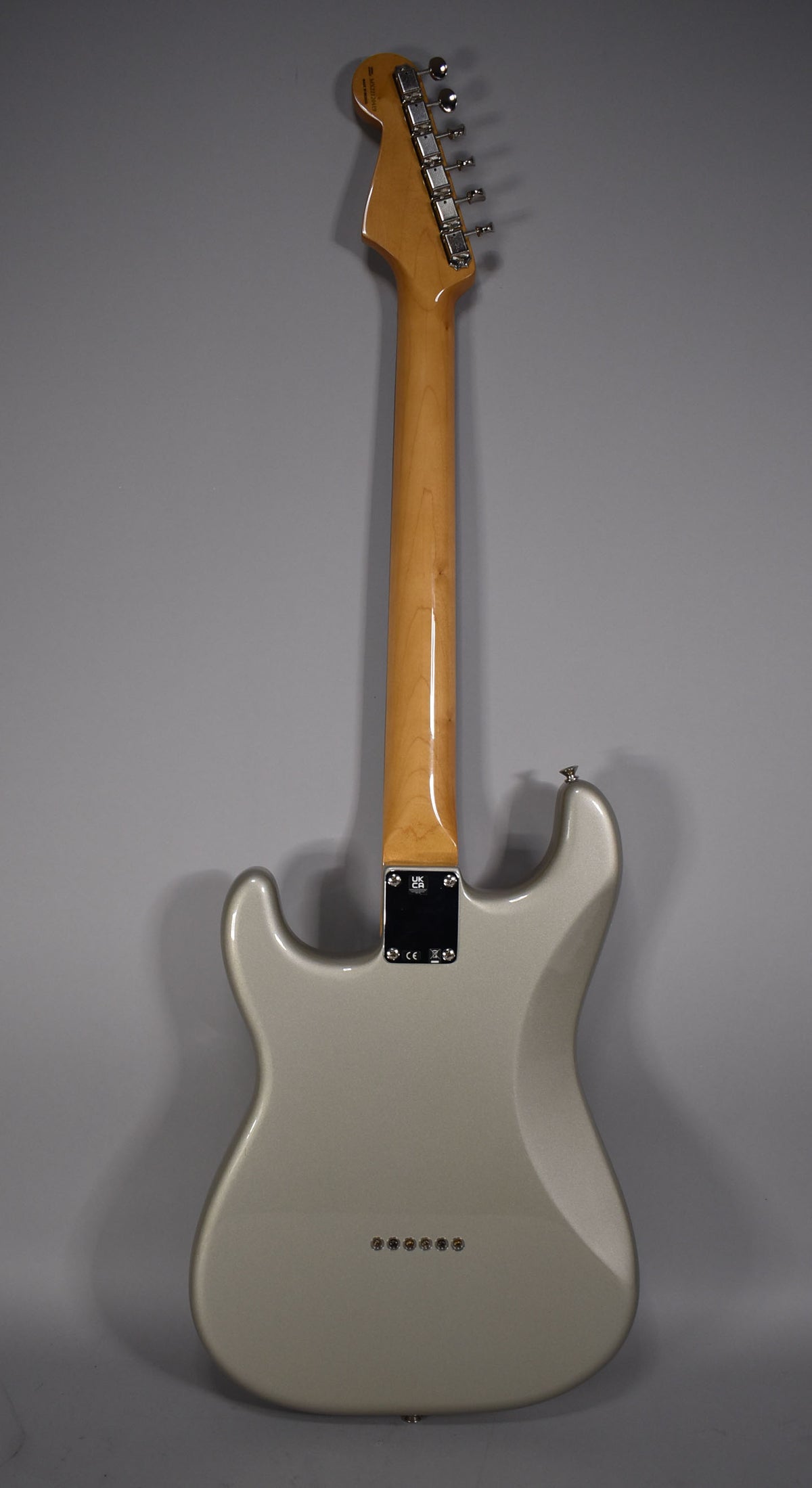 Full rear view of a metallic silver Stratocaster with a glossy amber neck, chrome tuners, and six string-through-body ferrules.