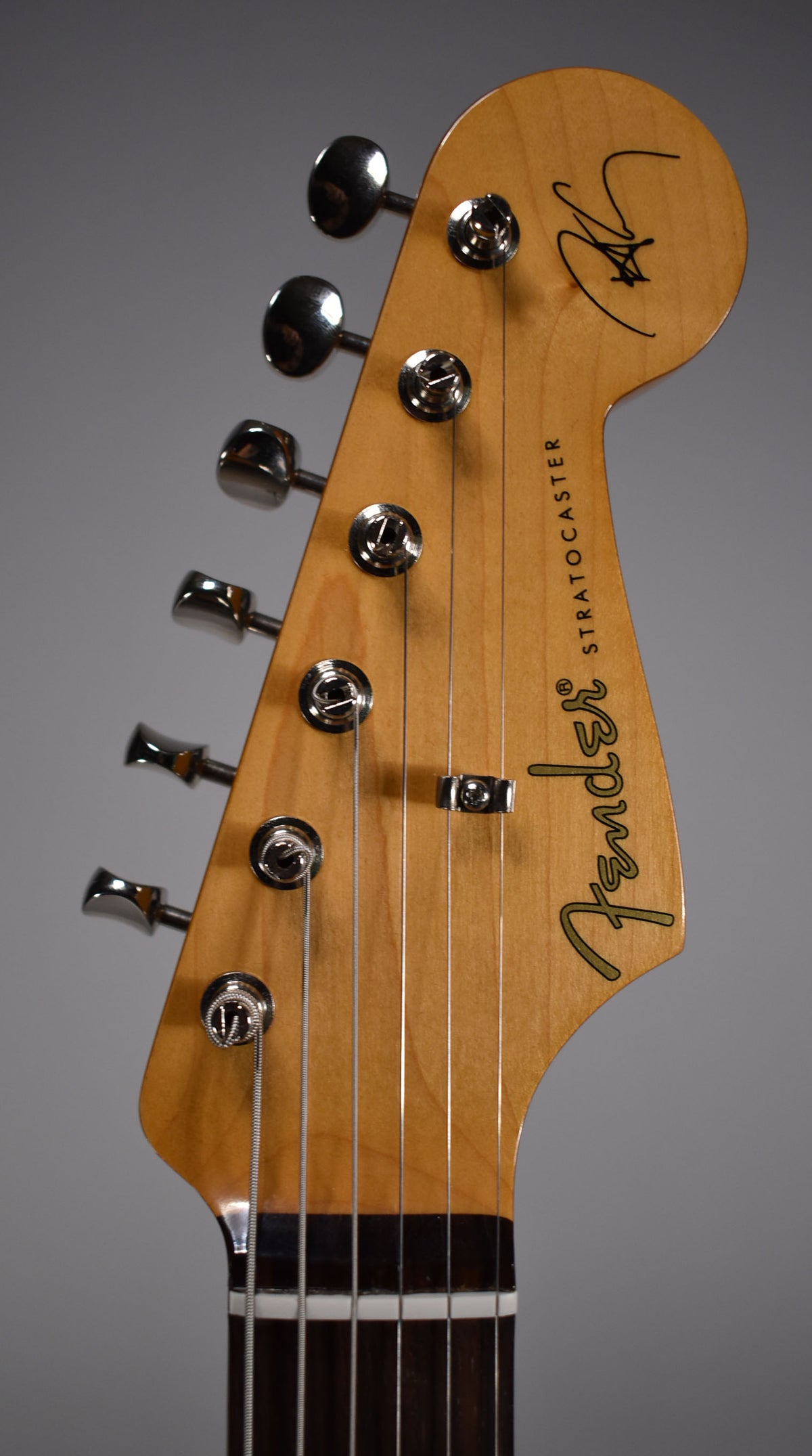 Close-up of the guitar's headstock, showing six chrome tuners, a string tree, and a dark fretboard with white frets.