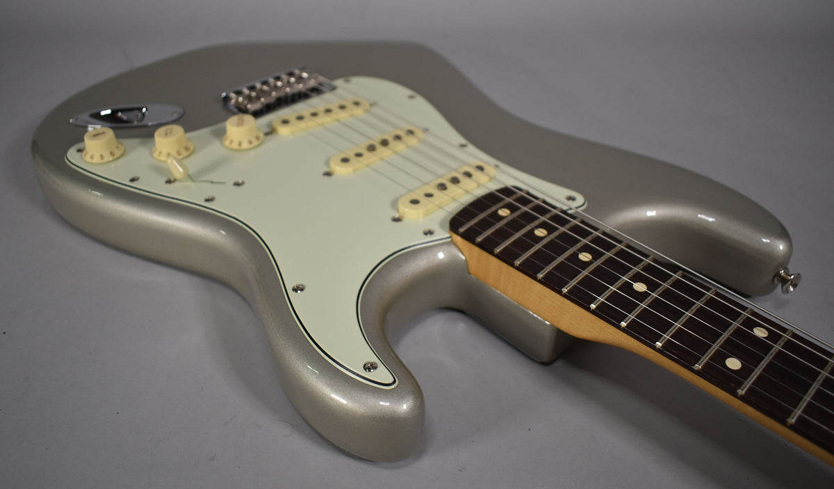 The Inca Silver Stratocaster body, with a white pickguard and aged cream controls, is angled from the lower left, showing the neck and fretboard.