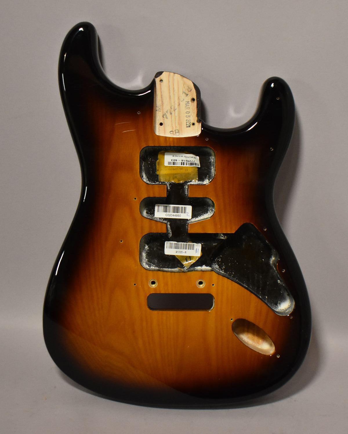 A glossy 2-tone sunburst Stratocaster body, viewed from the back, showing pickup cavities and a neck pocket with visible markings.