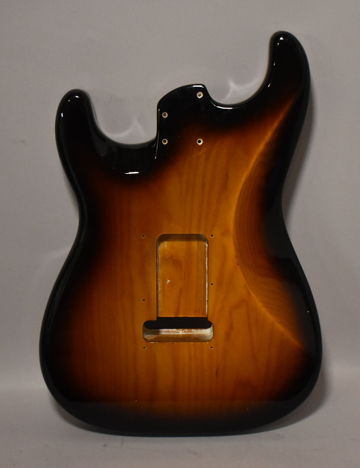 The glossy 2-tone sunburst Stratocaster body is viewed from the back, showing the tremolo cavity and neck pocket screw holes.