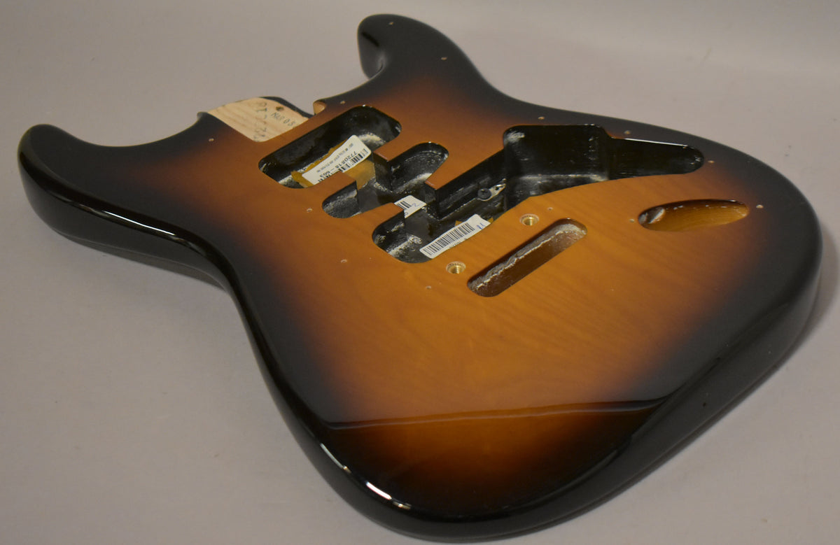 The Stratocaster body, in a glossy 2-tone sunburst, is angled to show the upper horn and three pickup cavities with visible labels.
