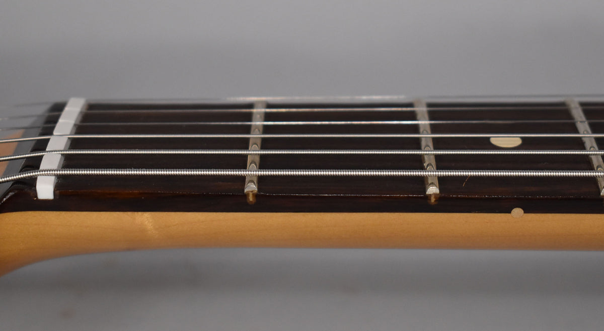 Close-up of the guitar's dark fretboard and light maple neck, showing the white nut, frets, strings, and a single fret marker.