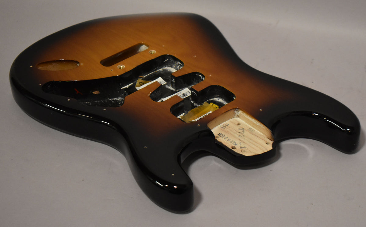 The guitar body, angled from the lower bout, shows a glossy 2-tone sunburst finish with routed cavities and a bare wood neck pocket.