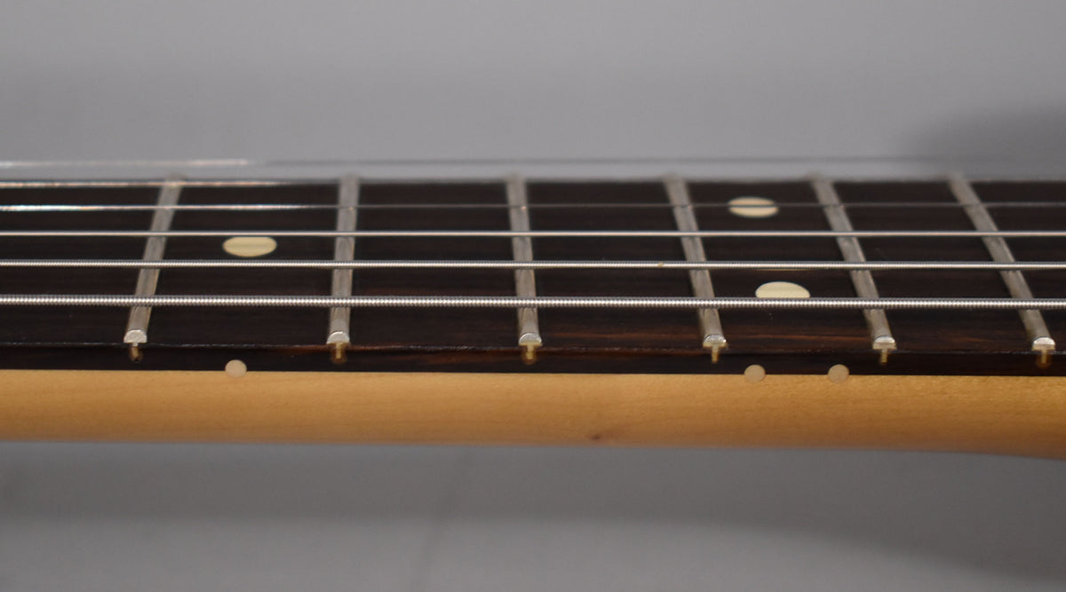 Close-up of the dark fretboard and light maple neck, showing the frets, strings, and cream dot inlays.
