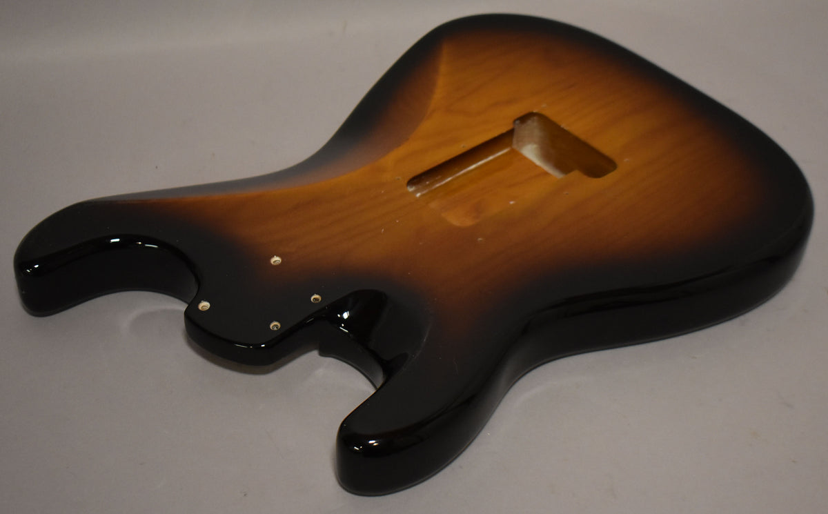 The Stratocaster body, in a glossy 2-tone sunburst, is viewed from the back, showing the neck pocket and string-through-body holes.